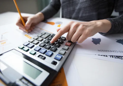 Close-up of female hand counting with calculator, papers all around on table. Businesswoman working with documents