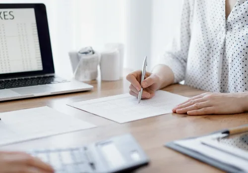 Two accountants using a laptop computer and calculator while counting taxes at wooden desk in office. Teamwork in business audit and finance.
